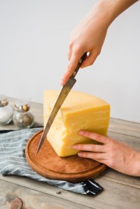 close-up-person-cutting-cheese-with-knife-round-chopping-board_23-2148166558